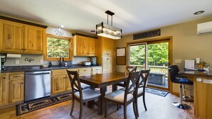 A kitchen with wooden cabinets, a dining table with chairs, a coffee station, and a view through large windows.