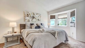 A bedroom with a bed, two bedside tables, a window with blinds, and a ceiling fan.