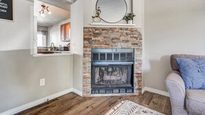 A living room with a stone fireplace, a mounted mirror, and a grey sofa.