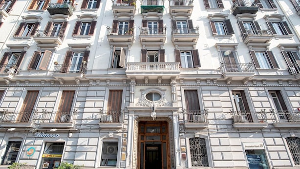 Um edifício de vários andares com entrada central, varandas e uma placa com 'Vilanova'.