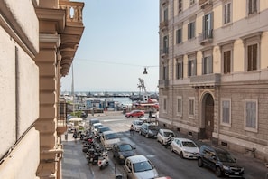 A street with parked cars and a view of a marina in the background.