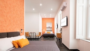 A hotel room with a large bed, a small table, two chairs, a sofa, a TV, and a window. - Napul 19 - Quadrupla (Naples)