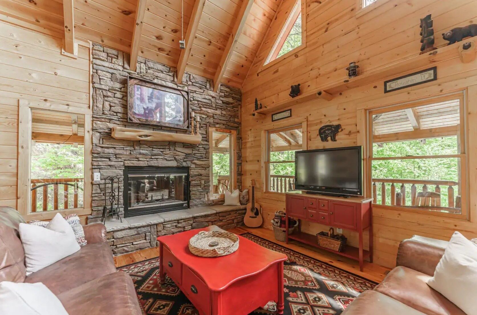 L’intérieur d’un chalet chaleureux, avec une cheminée en pierre, un téléviseur et une table basse rouge.