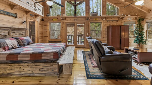 A log cabin interior with a large bed, a leather sofa, and a dining area. - Powdermill Hill Cabin 3 Bedroom Cabin by RedAwning (Gatlinburg)