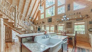 A rustic cabin interior with a kitchen featuring a large granite countertop sink, wooden floors, and a dining area with a view of the outdoors. - Powdermill Hill Cabin 3 Bedroom Cabin by RedAwning (Gatlinburg)