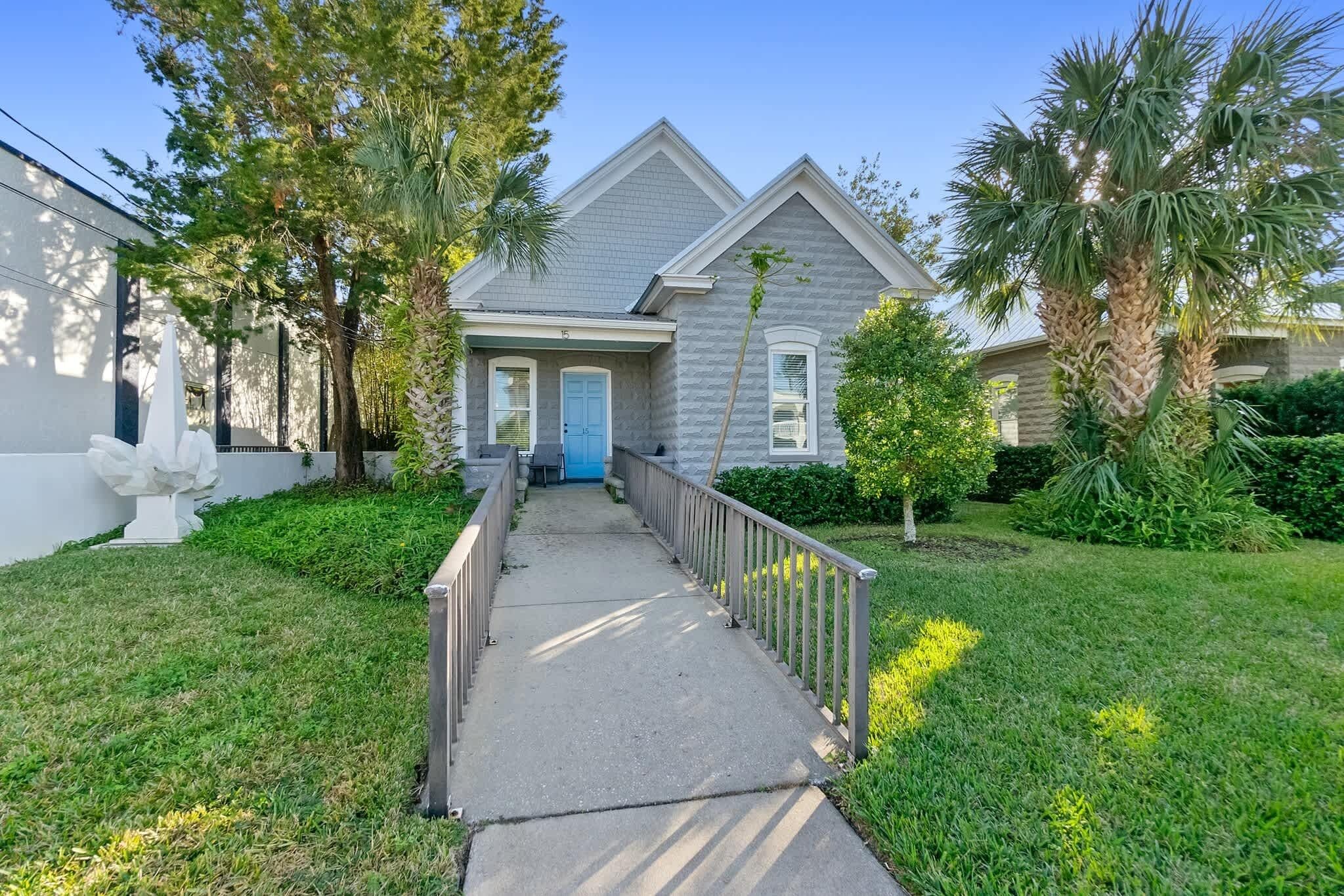 A residential house with a covered walkway, a blue door, and a well-maintained lawn with palm trees.