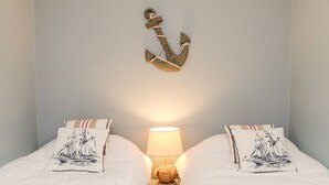 Un lit double avec des oreillers assortis, une petite table de chevet avec une lampe et une décoration murale en forme d’ancre.