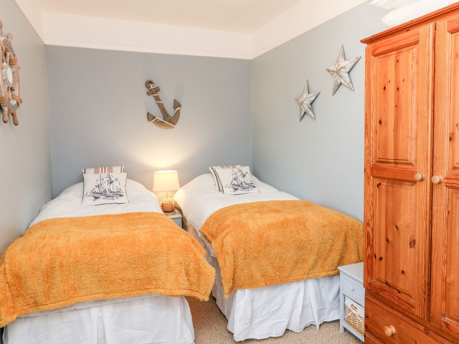 A bedroom with two beds, a wooden wardrobe, and nautical-themed decor.