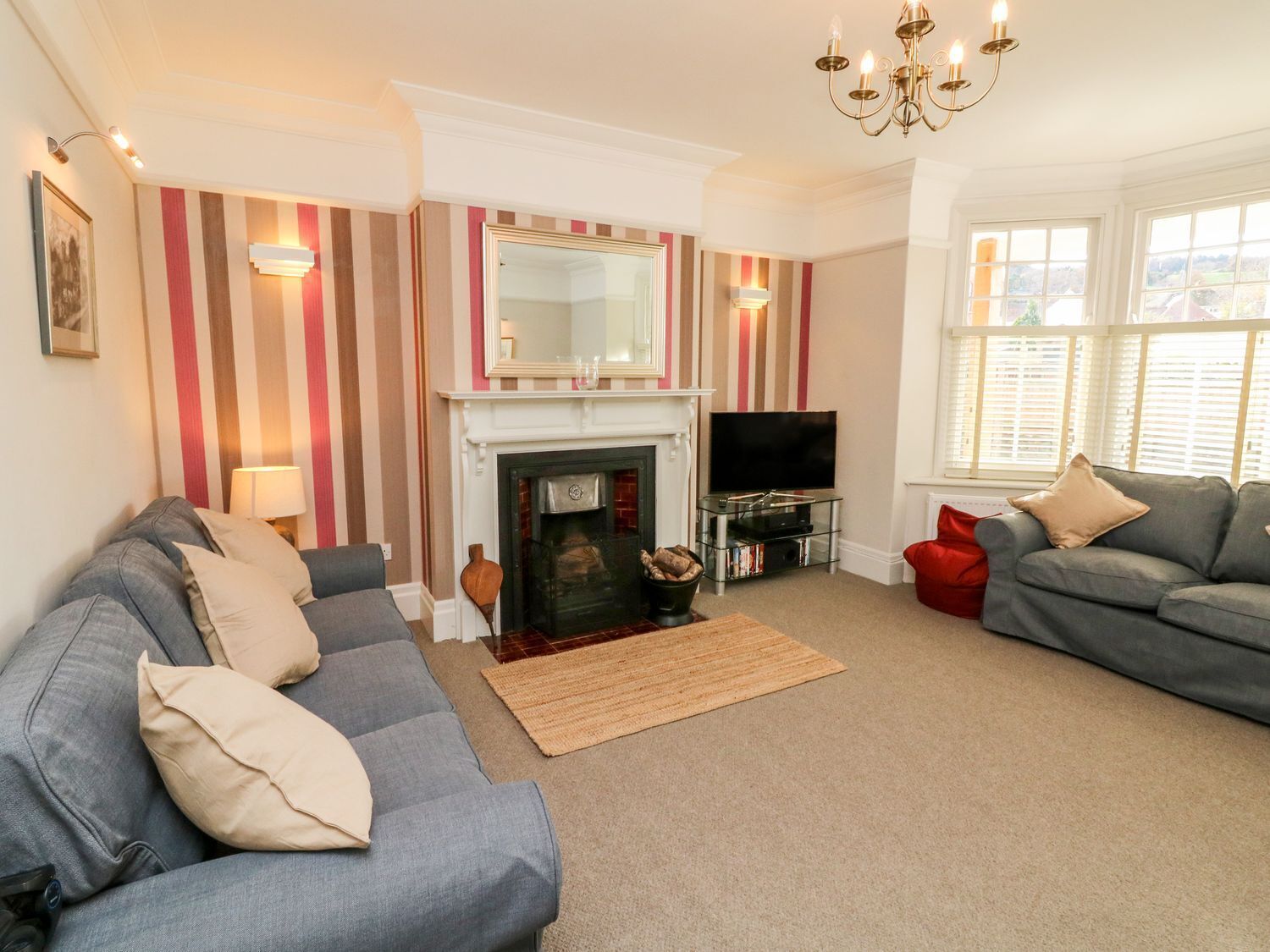 A living room with a fireplace, two sofas, a TV, and striped wallpaper.