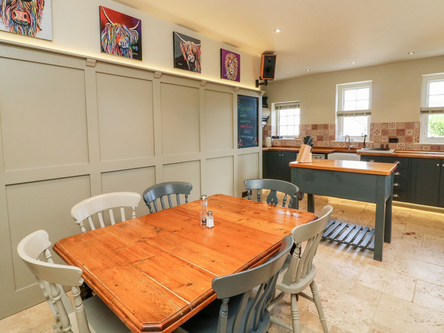 A dining area with a wooden table and chairs, a kitchen with a tiled backsplash, and artwork on the wall.