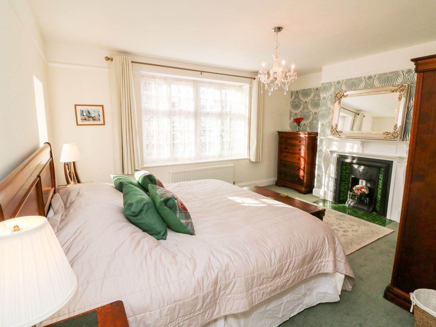 A bedroom with a large bed, a dresser, a mirror, a fireplace, and a chandelier.