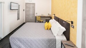 A hotel room with a bed, a desk, and a TV mounted on the wall.