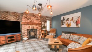 A living room with a brick fireplace, a television, a sofa, and a patterned rug. - Well Cottage (Beverley)