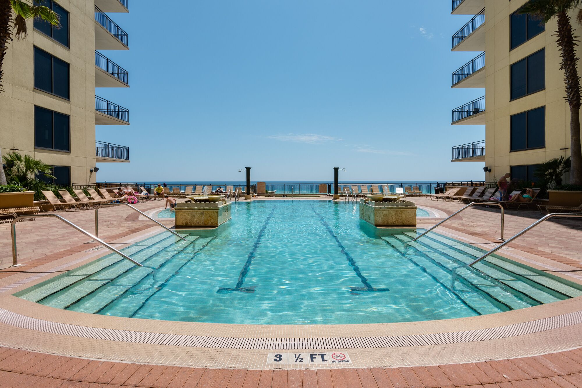 A swimming pool with a 3 1/2 ft depth limit, surrounded by lounge chairs and a view of the ocean.
