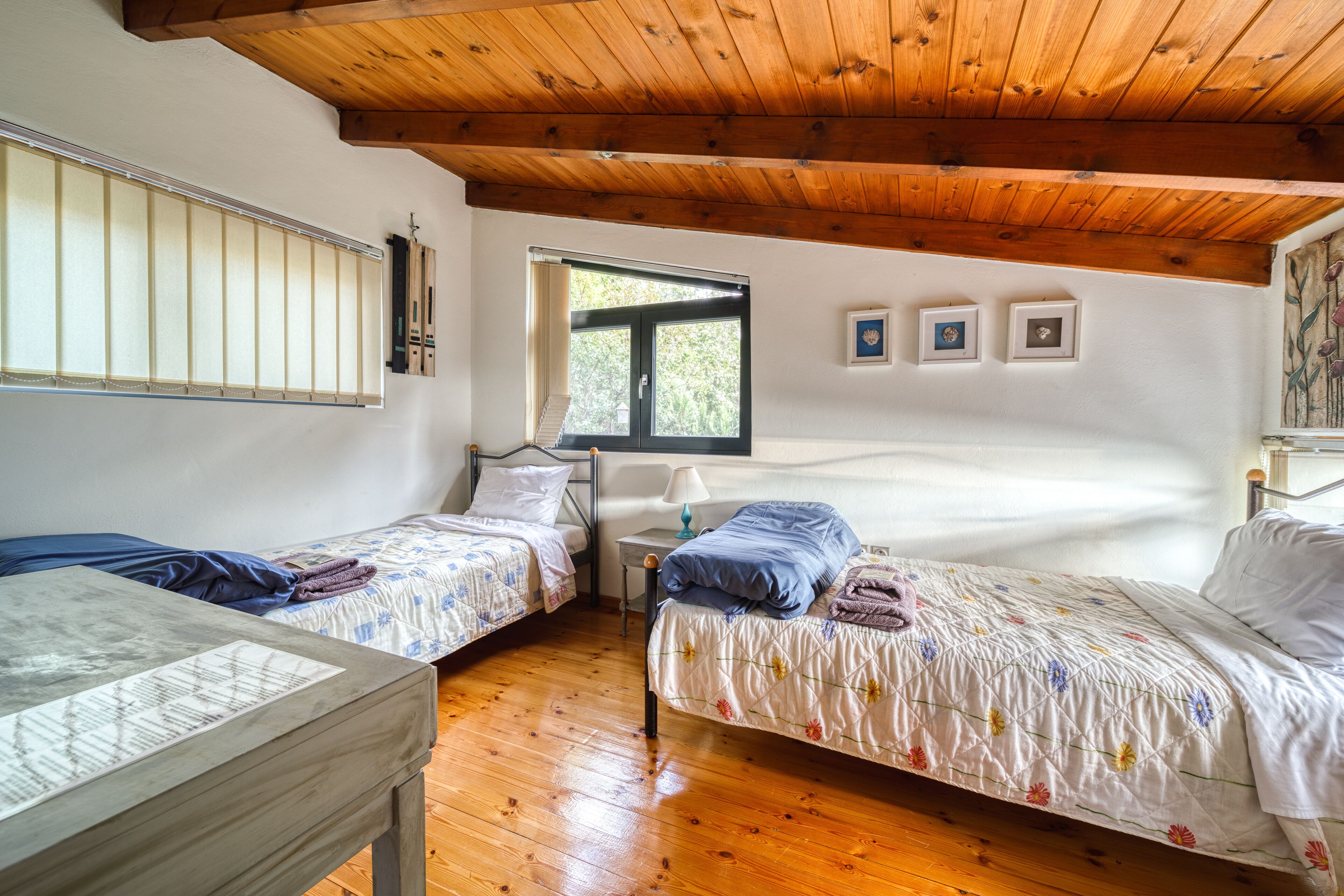 Una stanza con due letti singoli, pavimento in legno, soffitto in legno, una finestra e quadri appesi al muro.