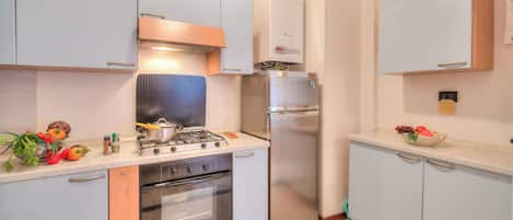 A compact kitchen with a gas stove, oven, and a stainless steel refrigerator.