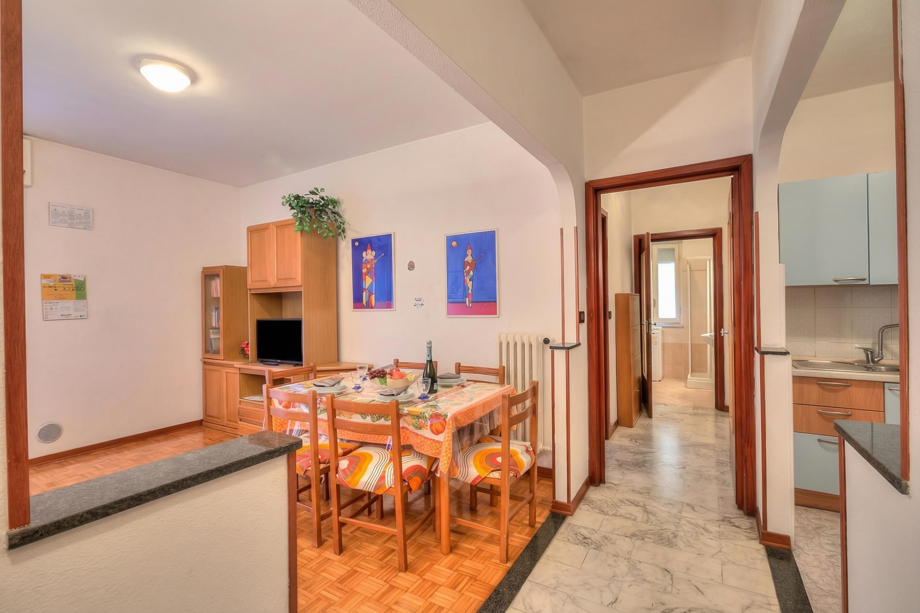 A dining area with a wooden table and chairs, a television, and artwork on the walls.