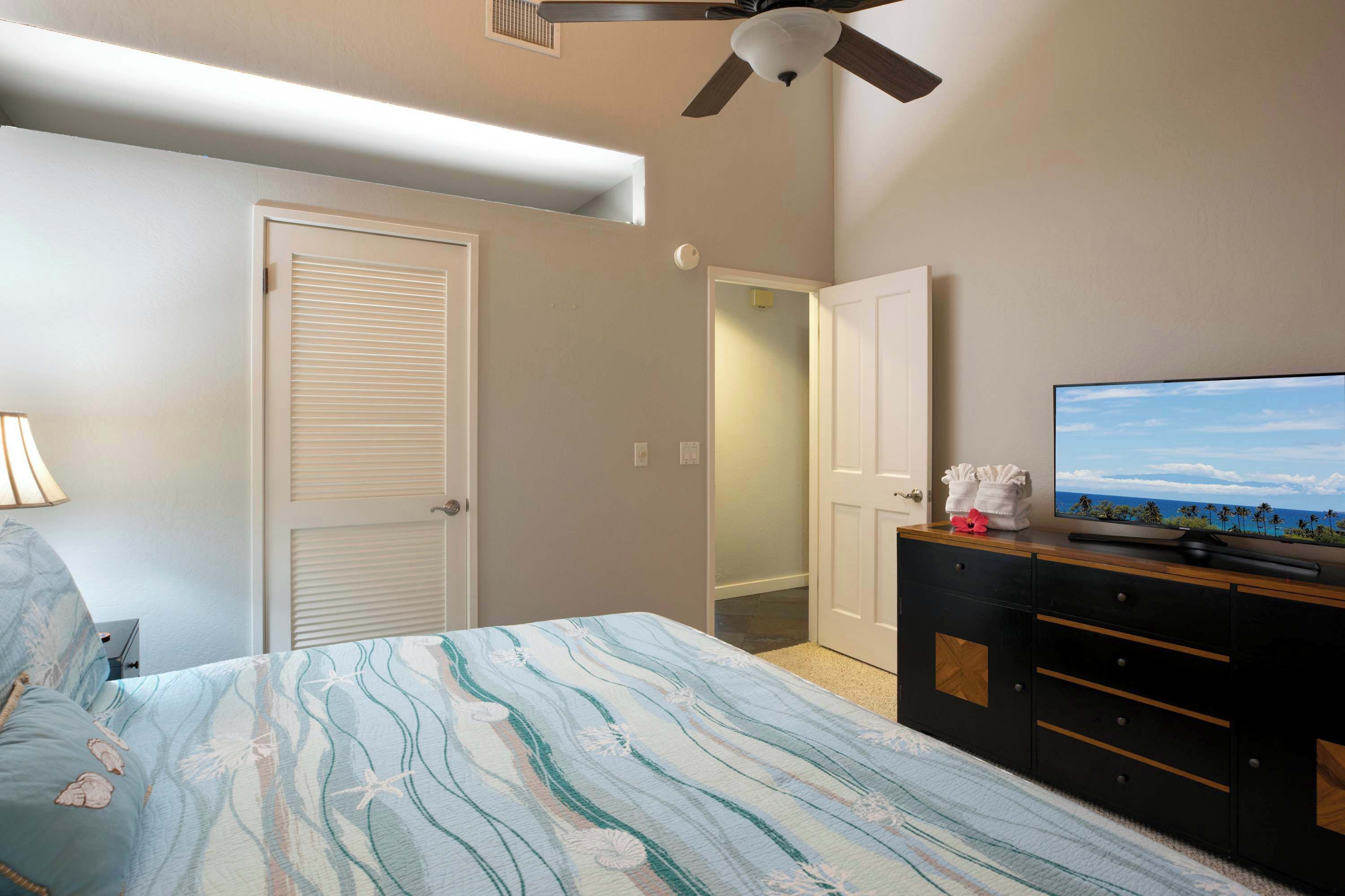 Un dormitorio con cama, televisor sobre una cómoda y ventilador de techo.