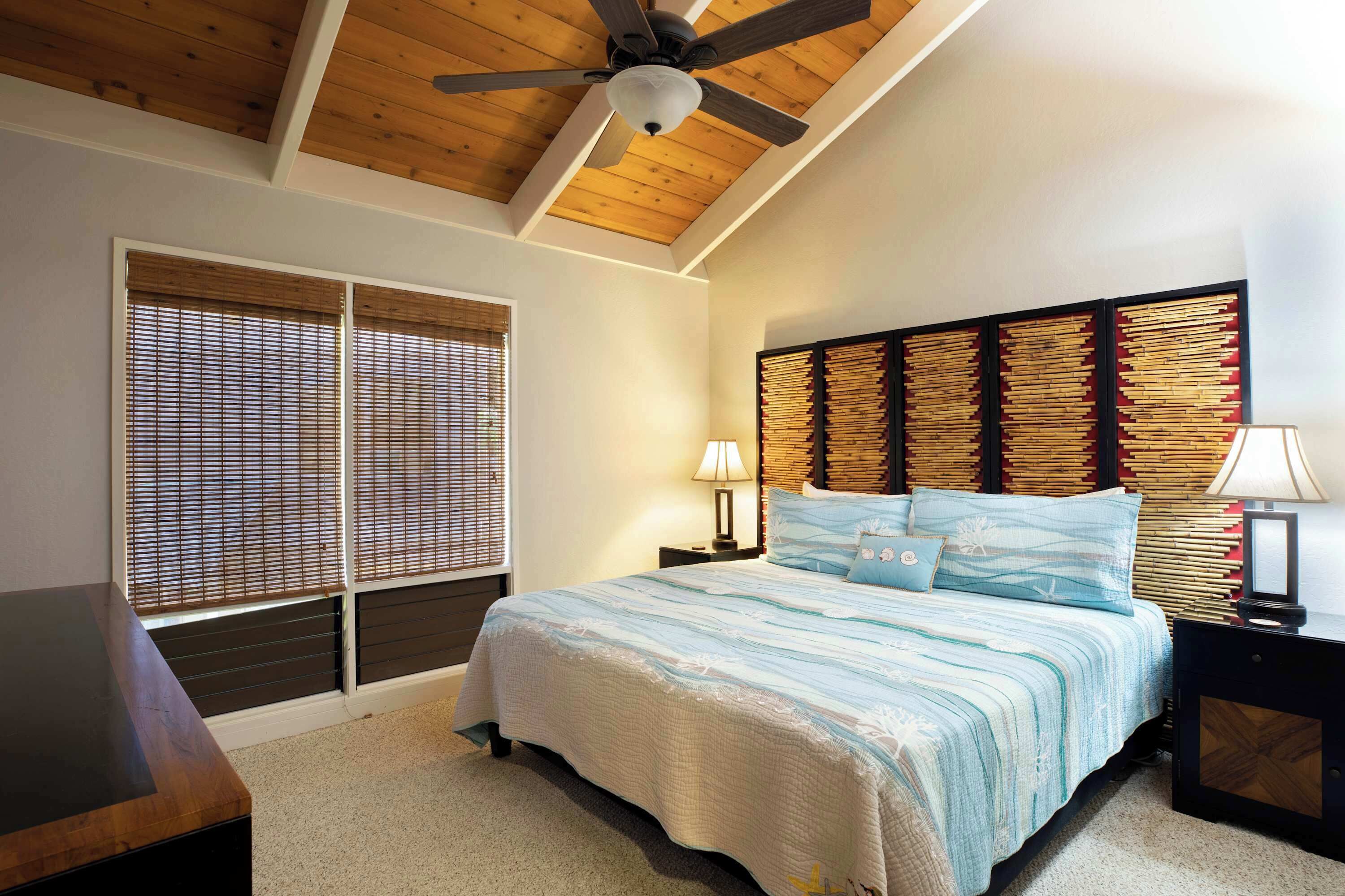 A bedroom with a bed, wooden ceiling, and a nightstand with a lamp.