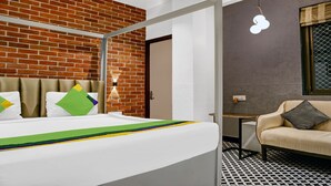 A hotel room with a brick wall, a bed with colorful pillows, a small table, a chair, and a unique light fixture. - Itsy Hotels Banana Boutique (Varanasi)
