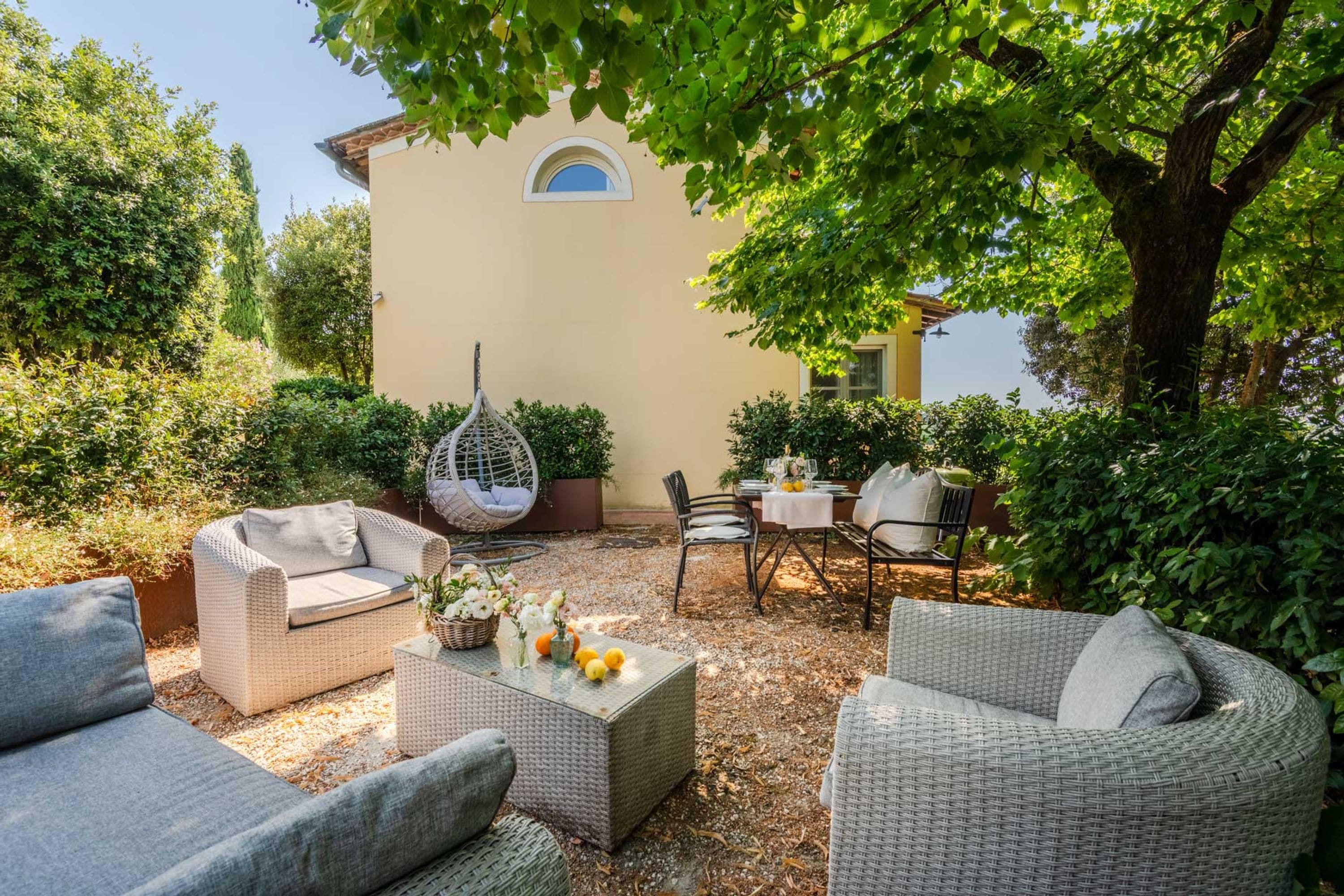 Une terrasse extérieure aménagée avec des meubles en osier, un fauteuil suspendu et une table dressée pour le repas.
