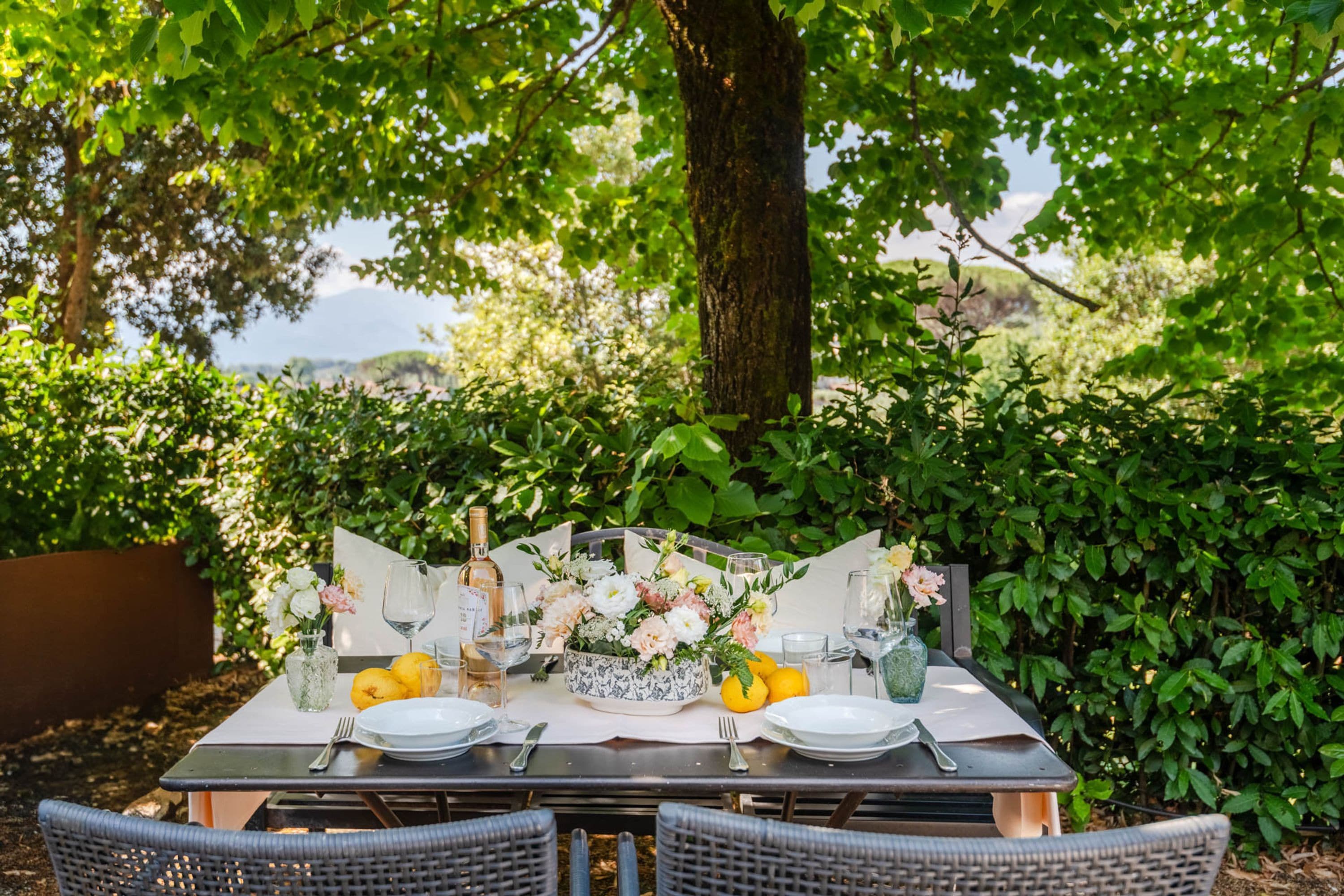 An outdoor dining table set with plates, cutlery, glasses, and a centerpiece of flowers and lemons.