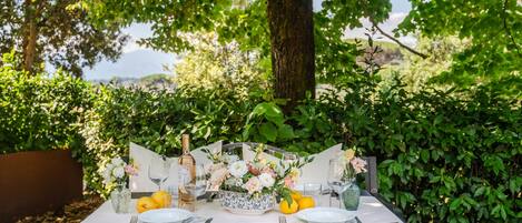 An outdoor dining table set with plates, cutlery, glasses, and a centerpiece of flowers and lemons.