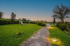 A gravel path leading through a grassy area with a playground and a tree.