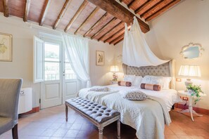 A bedroom with a large bed, a bench, two bedside tables, and a canopy bed.