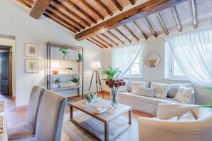 A living room with a wooden ceiling, a sofa set, a coffee table, and a bookshelf with plants. - Maria Farmhouse Apartment in Wine Resort in Lucca (Lucca)