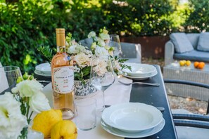 An outdoor dining table set with a bottle of Fattoria Sardi wine, glasses, plates, and a centerpiece of flowers.