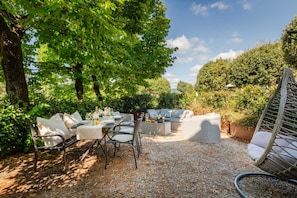 An outdoor seating area with a table, chairs, and a hanging chair, surrounded by trees and greenery.