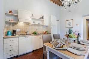Uma cozinha com armários brancos, painel de azulejos e uma mesa de jantar de madeira posta com pratos, copos e uma cesta de pão.