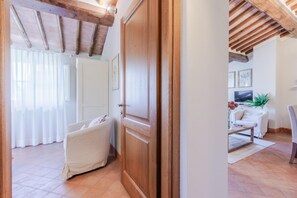 Quarto com porta de madeira, sofá branco, televisão e uma planta.
