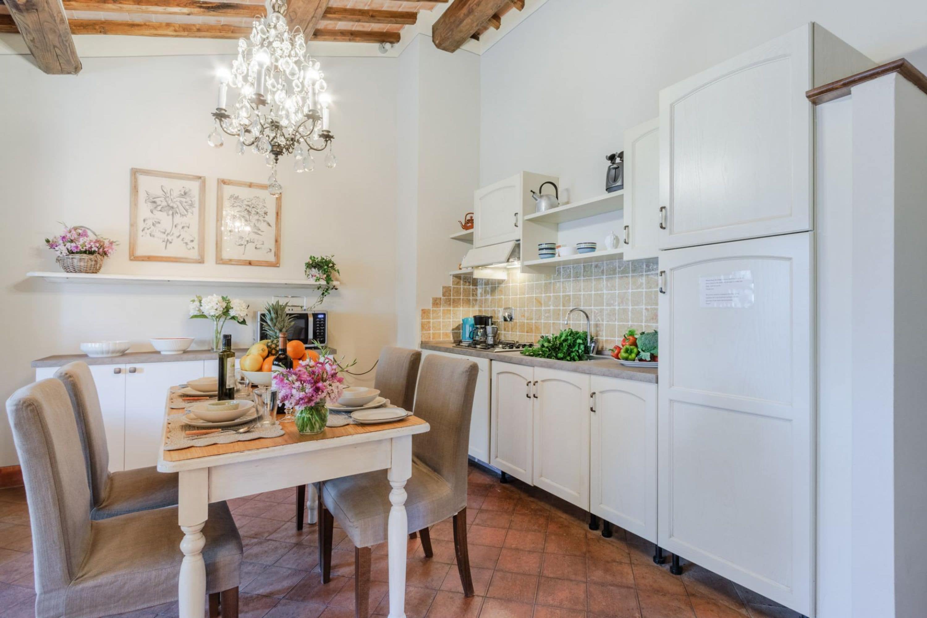 A kitchen with white cabinets, a wooden dining table, and a chandelier.