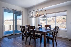 A dining room with a large table and chairs, a chandelier, and large windows with a view of a mountainous landscape. - Powder Ridge Escape T4 | Mtn Biking | Hot Tub (Eden)