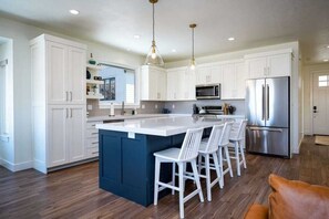 A modern kitchen with white cabinets, a central island with bar stools, stainless steel appliances, and pendant lighting.