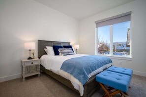 A bedroom with a bed, bedside tables, a bench, and a window with a view. - Powder Ridge Escape T4 | Mtn Biking | Hot Tub (Eden)