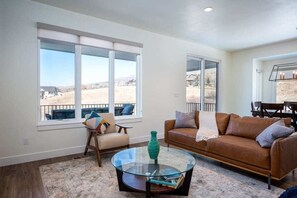 Relax in a spacious living room with a large window offering a view, a comfortable sofa, and a dining area.