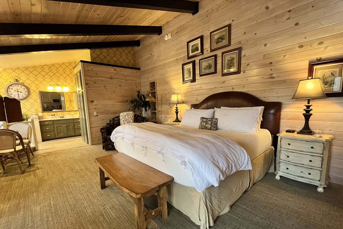 Un dormitorio acogedor con cabecera de madera, un banco de madera, una mesita de noche con lámpara y un reloj de pared.