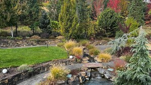 Un jardin avec un étang, des murs en pierre et différentes espèces de plantes.
