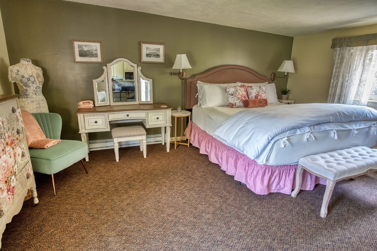 Un dormitorio con cama, tocador con espejo, cómoda, silla y banco.