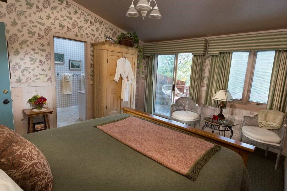 Un dormitorio con cama, armario de madera, una mesita de noche con lámpara y una silla.