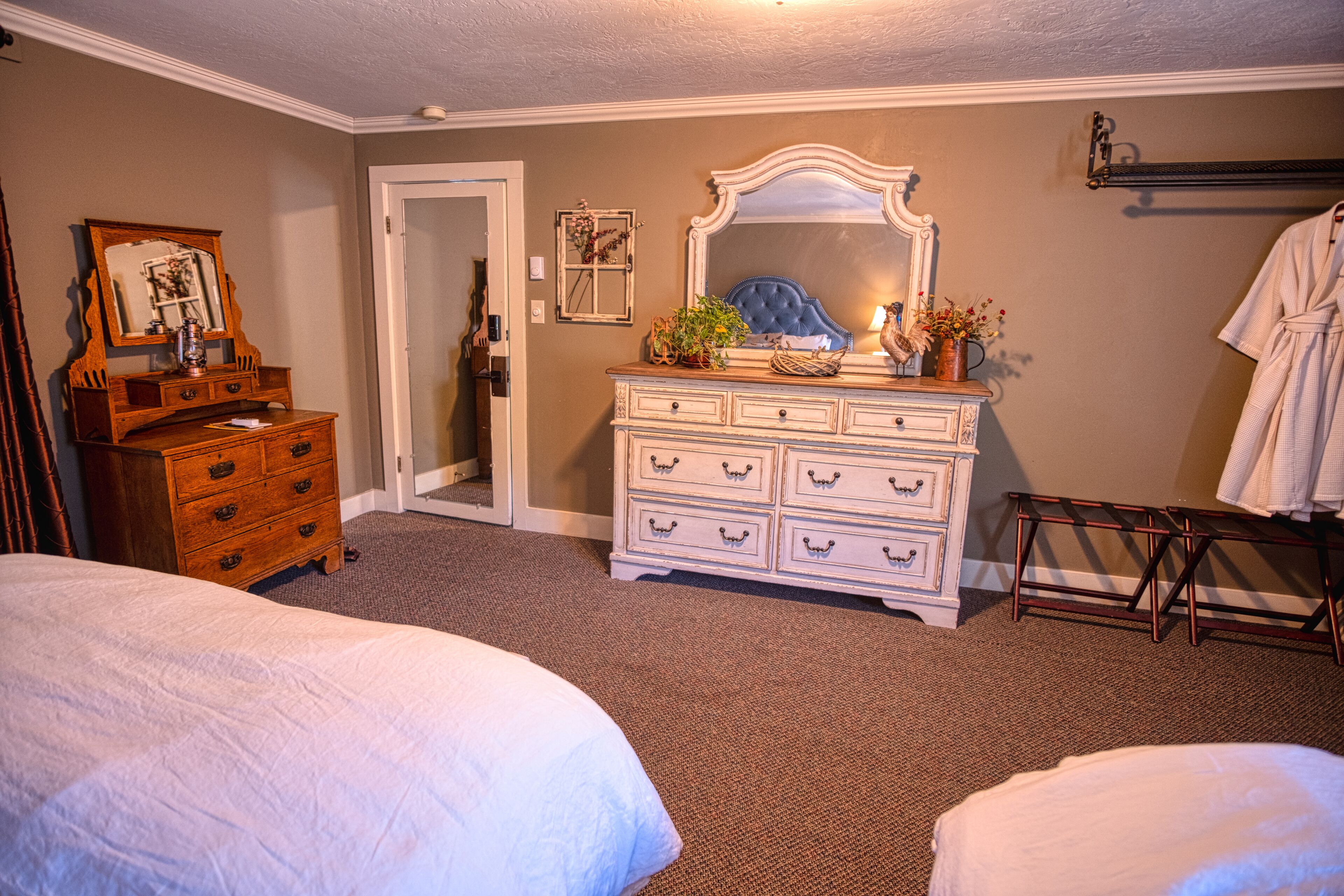 A bedroom with two beds, a dresser with a mirror, a vanity with a mirror, and a robe hanging on a rack.