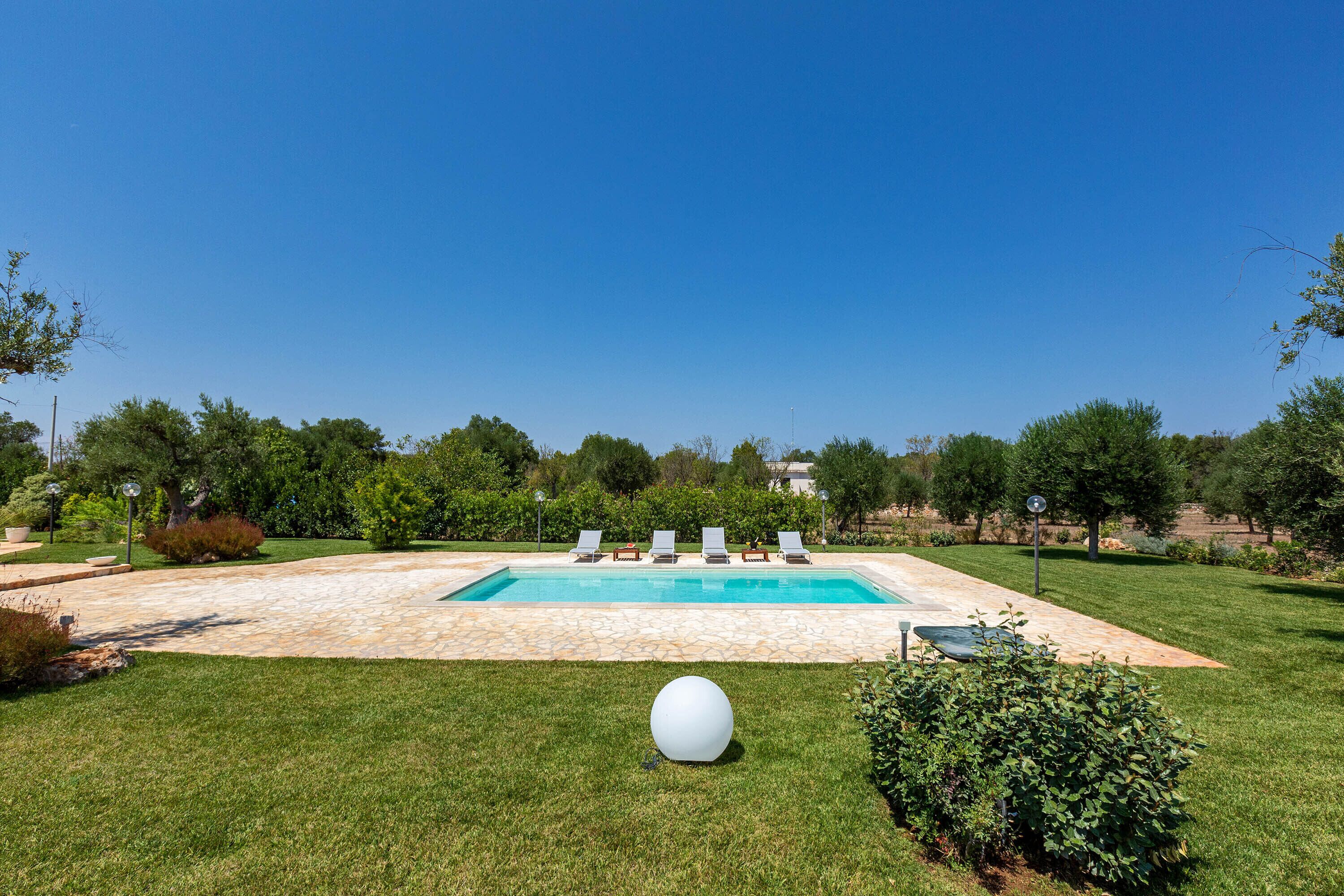 A swimming pool with four lounge chairs and a white spherical object in the foreground.