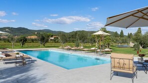 A swimming pool with lounge chairs and umbrellas, surrounded by greenery and hills. - La Buganvilla 14 (Campiglia Marittima)