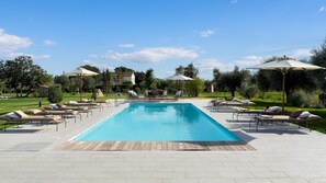 A rectangular swimming pool with lounge chairs and umbrellas, surrounded by a paved deck and greenery. - La Buganvilla 14 (Campiglia Marittima)