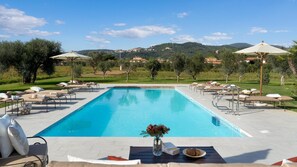 A rectangular swimming pool with lounge chairs and umbrellas, surrounded by greenery and hills in the background. - La Buganvilla 14 (Campiglia Marittima)