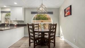 A modern kitchen with a dining area, featuring a round table with chairs, a pendant light, and a view of greenery through a window. - Cozy 2 bedroom house in Chandler (Chandler)