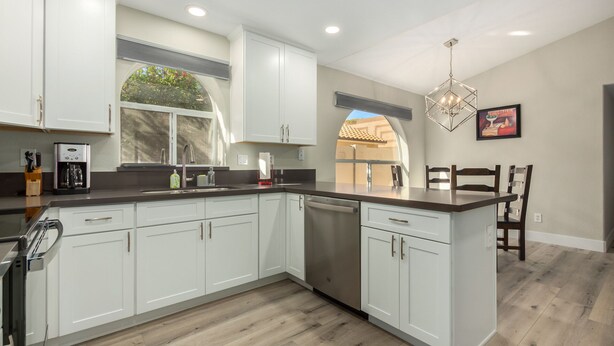 A modern kitchen with white cabinets, a built-in dishwasher, and a large island with a dark countertop. - Cozy 2 bedroom house in Chandler (Chandler)